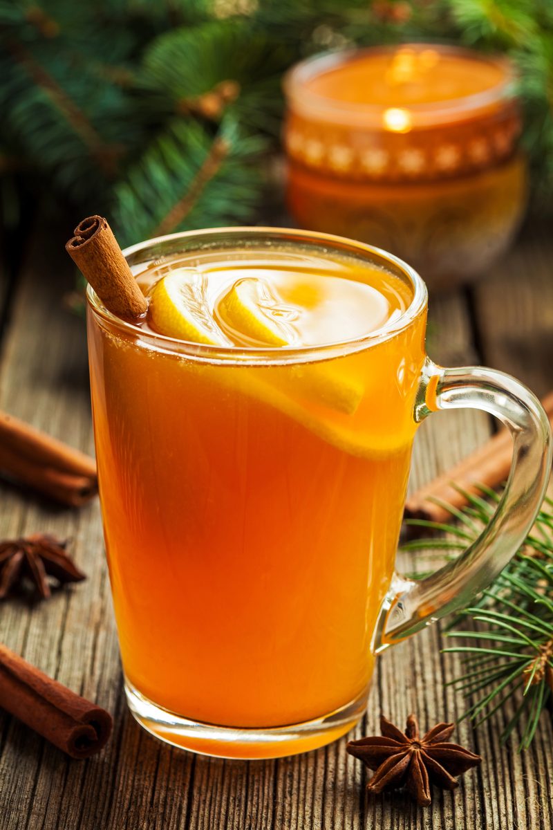 Glass mug of hot whiskey with lemon and spices by candlelight