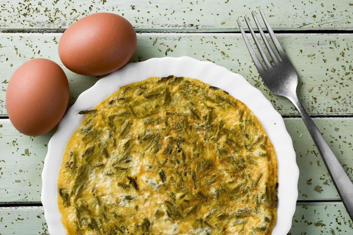 Wild asparagus omelet in a white dish with eggs alongside