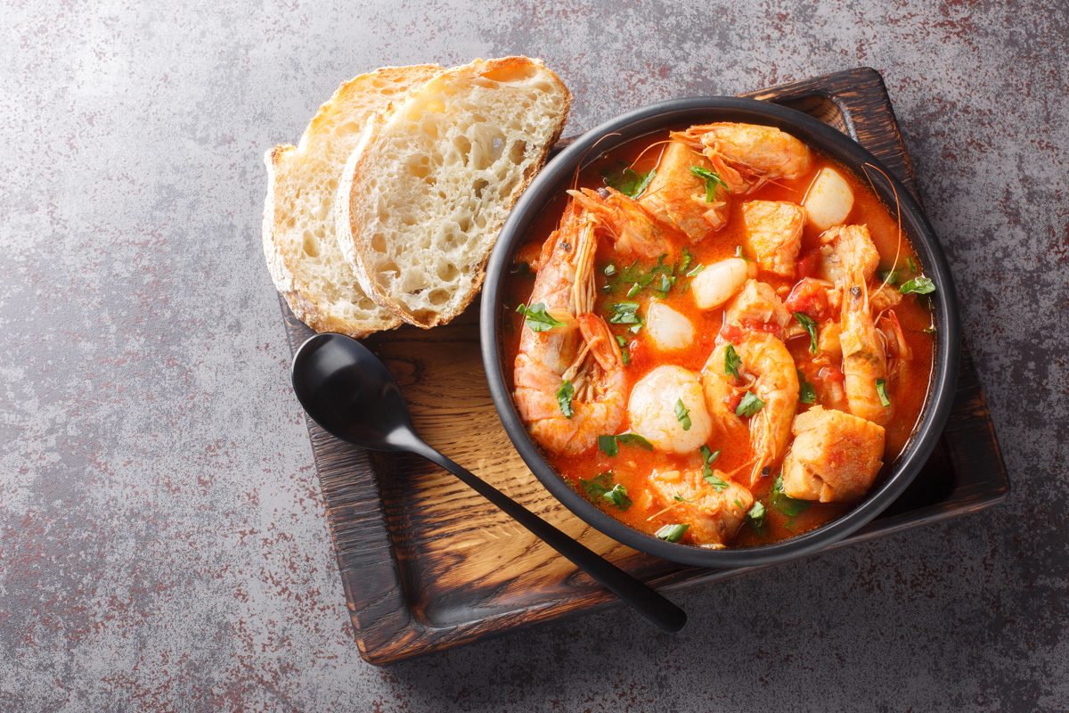 Dalmatian fish stew with tomato in a dark bowl, with bread