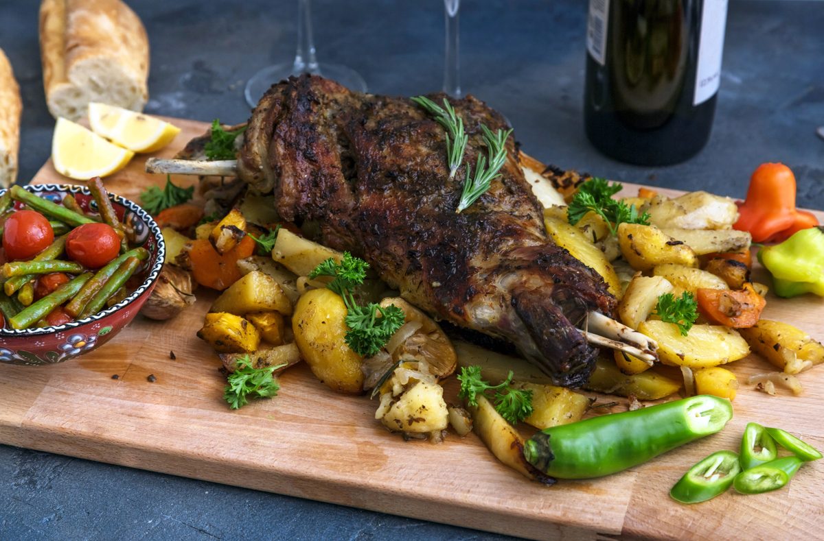 Roast lamb shoulder with roasted potatoes and vegetables on a board
