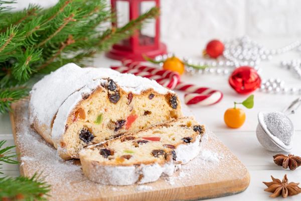 Christstollen dusted with powdered sugar, sliced to show dried fruit, on a board with Christmas decorations