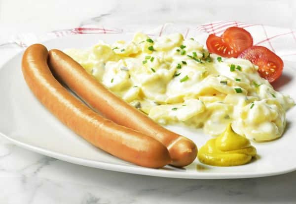 German potato salad with two sausages and mustard on a white plate