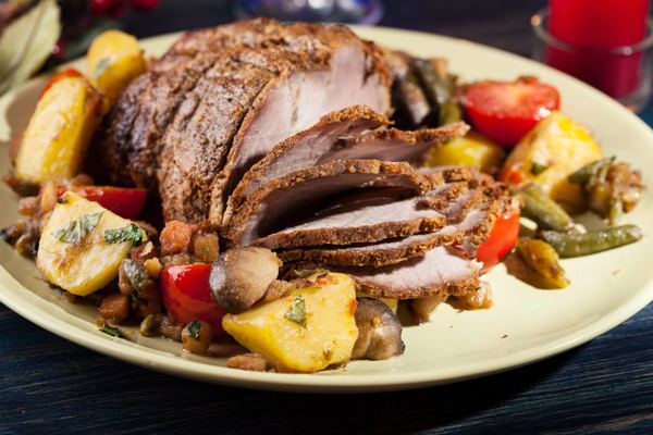 Sliced roast pork with roasted vegetables on a holiday platter