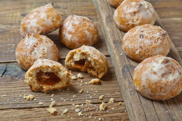 Small round spiced cookies on a wooden table, one broken to show the filling