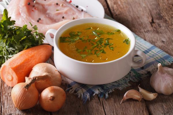 Bowl of clear chicken consommé with carrots and onions on the table