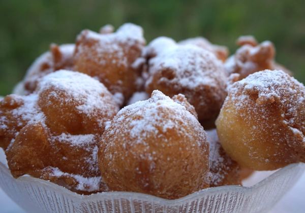 Fritule, small fried dough balls dusted with powdered sugar, in a glass bowl