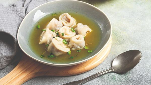 Small meat-filled pasta in clear chicken broth, in a bowl with a spoon