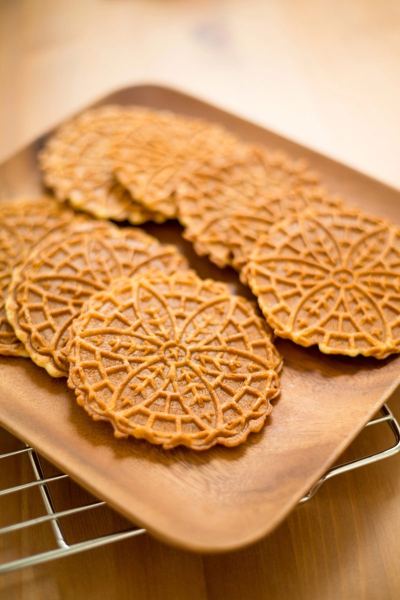 Thin patterned pizzelle wafer cookies on a wooden tray