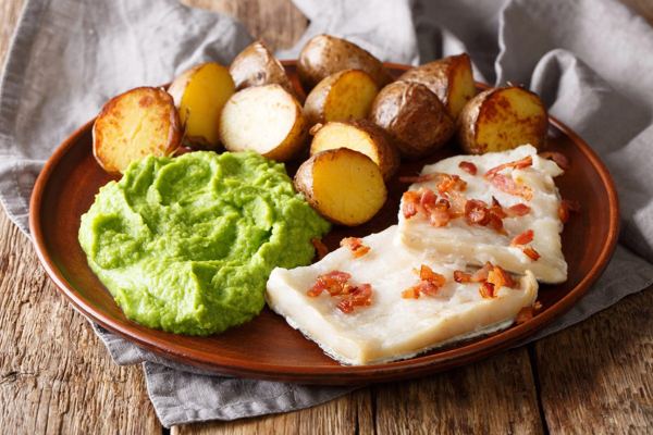 Lutfisk with green pea purée, boiled potatoes and bacon on a plate