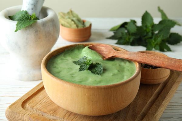 Bowl of creamy green nettle soup garnished with fresh nettle leaves