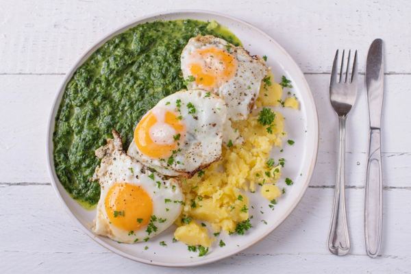Creamed spinach with two fried eggs and potatoes on a white plate