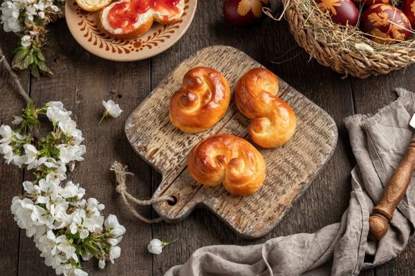 Golden spiral-shaped Judas buns on a wooden board with spring blossoms