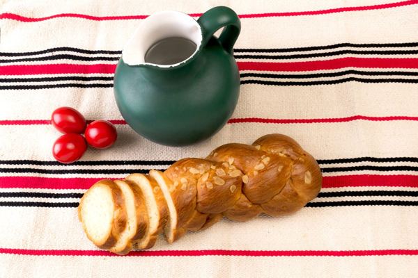 Sliced braided tsoureki Easter bread with red eggs and a green pitcher