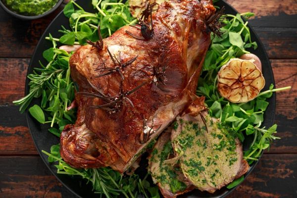 Roast leg of lamb with mint sauce, rosemary and garlic on salad leaves