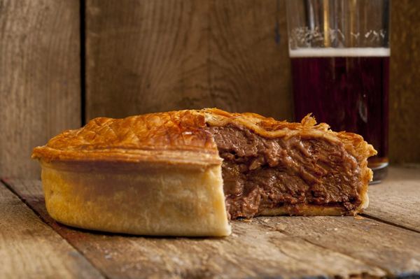 Beef pie with a slice cut out, next to a glass of dark beer
